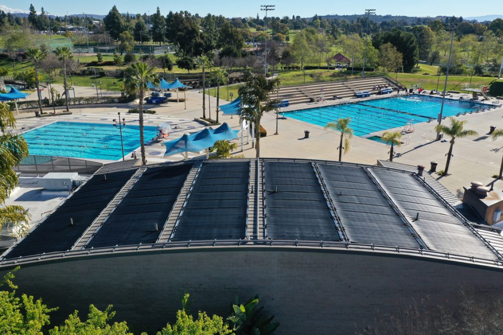 Commercial swimming pool with rooftop solar pool heating system installed, showcasing hybrid energy efficiency and extended swim season benefits.